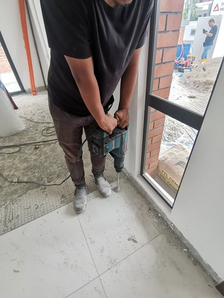 师傅在施工中建筑的门口位置，沿地台边缘钻孔。