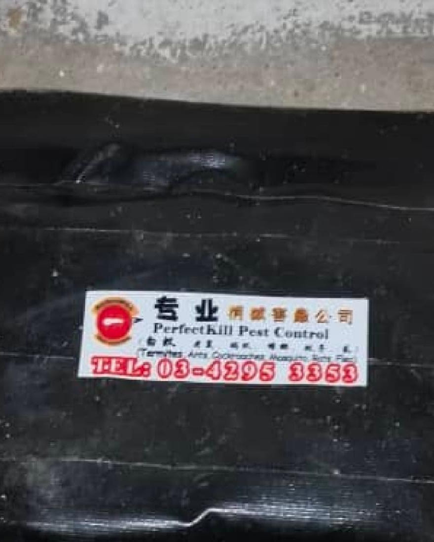 Perfect Kil 的黑色白蚁诱饵站，放在墙边地上，贴着公司印制的标签和办公室电话 03-4295 3353。